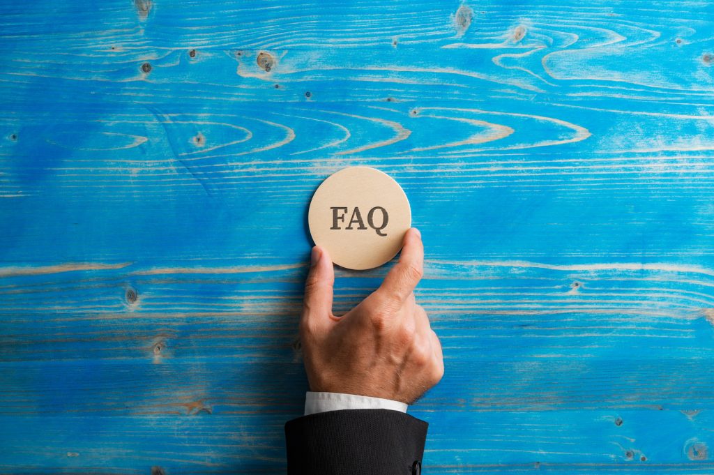 Hand of a businessman holding a wooden circle with FAQ sign on it